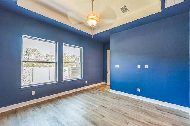 unfurnished room featuring ceiling fan, light wood-type flooring, and a raised ceiling