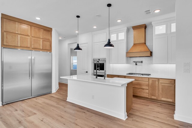 kitchen featuring white cabinetry, appliances with stainless steel finishes, custom exhaust hood, and an island with sink