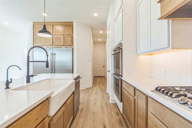 kitchen with appliances with stainless steel finishes, premium range hood, white cabinetry, decorative light fixtures, and tasteful backsplash