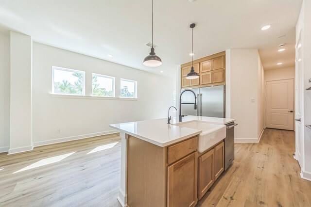 kitchen with hanging light fixtures, light wood-type flooring, appliances with stainless steel finishes, and a kitchen island with sink