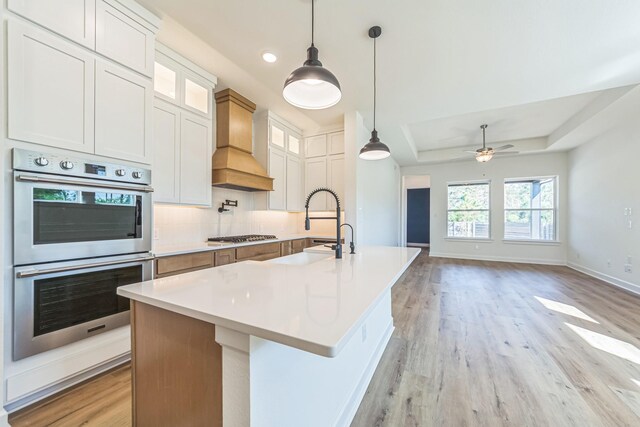 kitchen featuring appliances with stainless steel finishes, custom exhaust hood, a kitchen island with sink, and white cabinets