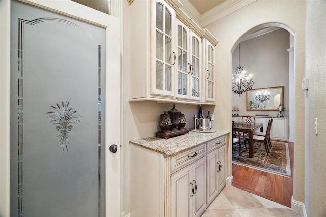 bar featuring light stone countertops, cream cabinets, decorative light fixtures, a notable chandelier, and crown molding