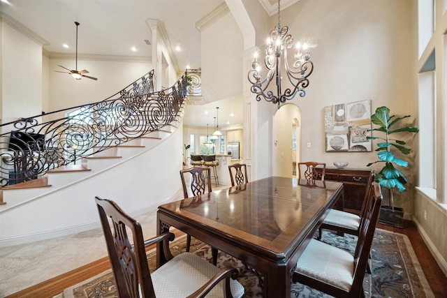 dining area with ceiling fan with notable chandelier, a towering ceiling, crown molding, and wood-type flooring