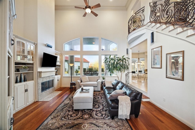 living room with dark wood-type flooring, a high ceiling, a premium fireplace, crown molding, and ceiling fan