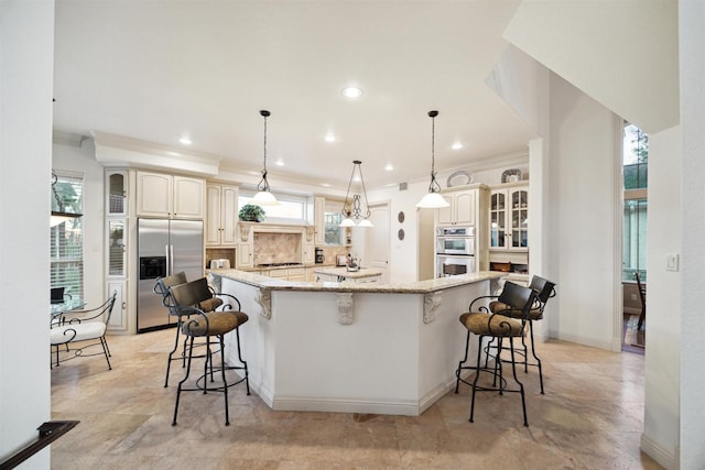 kitchen featuring stainless steel appliances, light stone counters, a spacious island, backsplash, and hanging light fixtures