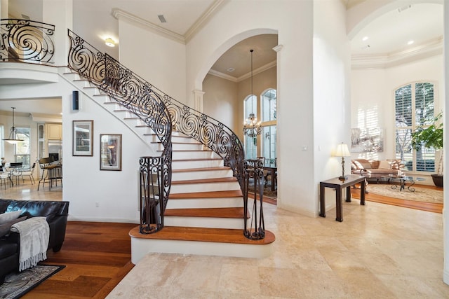 staircase with a towering ceiling, ornamental molding, a notable chandelier, and hardwood / wood-style flooring