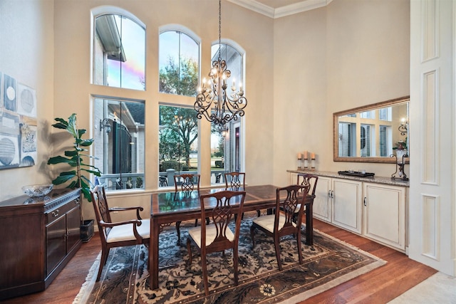 dining area with a high ceiling, hardwood / wood-style flooring, a notable chandelier, and ornamental molding