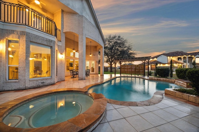 pool at dusk with ceiling fan, an in ground hot tub, a pergola, and a patio