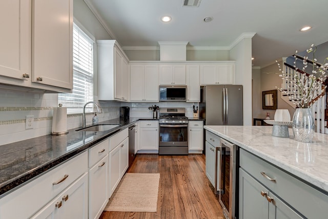 kitchen with appliances with stainless steel finishes, beverage cooler, white cabinets, and a sink