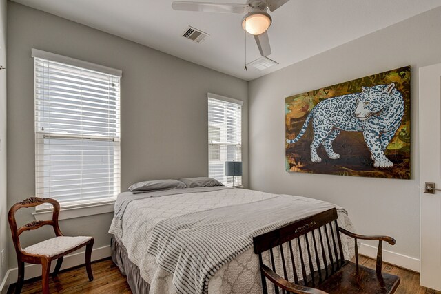 bedroom with a ceiling fan, wood finished floors, visible vents, and baseboards