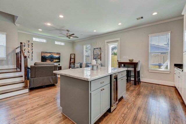 kitchen with a center island, visible vents, light wood-style floors, open floor plan, and light stone countertops