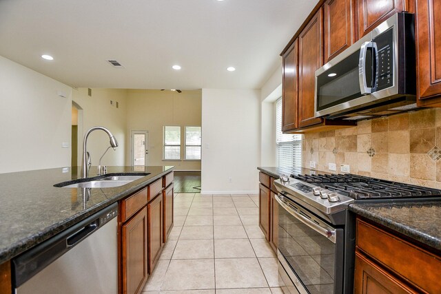 kitchen with a wealth of natural light, dark stone counters, stainless steel appliances, sink, and light tile patterned floors