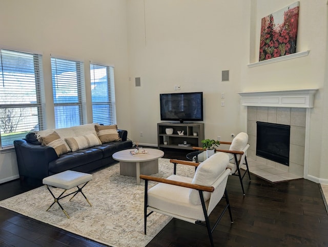 living room with a tile fireplace, hardwood / wood-style floors, a towering ceiling, and a healthy amount of sunlight