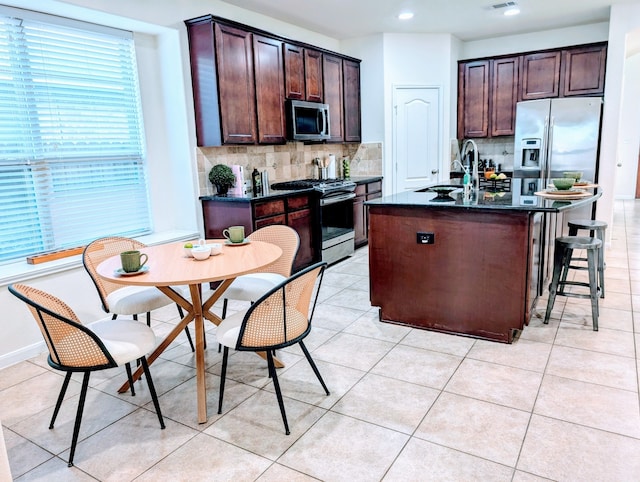 kitchen with decorative backsplash, stainless steel appliances, a kitchen island with sink, sink, and light tile patterned flooring