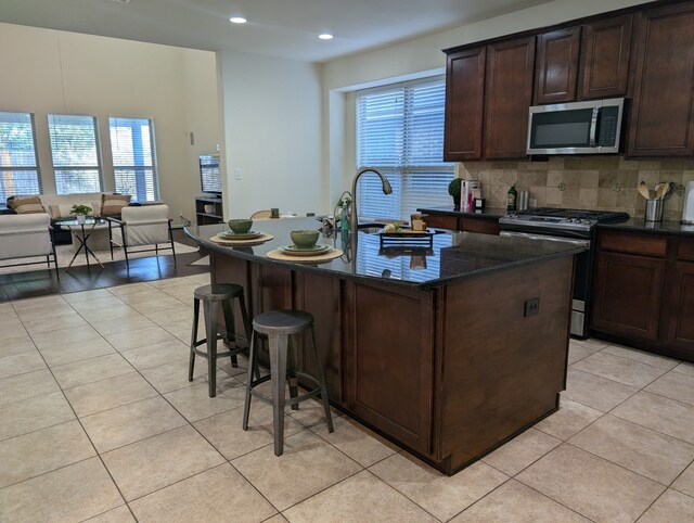 kitchen with a breakfast bar, light tile patterned floors, an island with sink, and appliances with stainless steel finishes