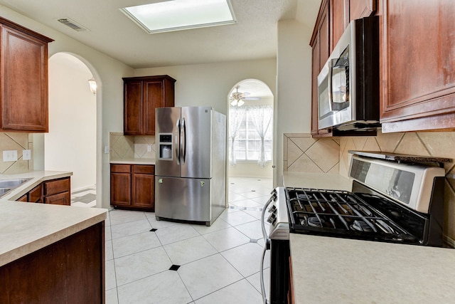 kitchen with ceiling fan, sink, stainless steel appliances, backsplash, and light tile patterned floors