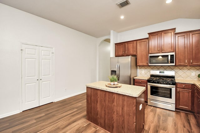 kitchen with decorative backsplash, appliances with stainless steel finishes, vaulted ceiling, a center island, and dark hardwood / wood-style floors