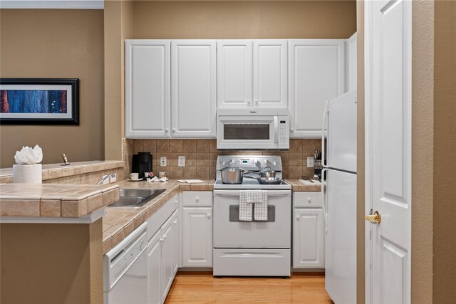 kitchen with kitchen peninsula, white appliances, white cabinets, and tasteful backsplash