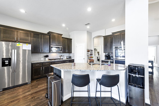 kitchen featuring dark wood-type flooring, sink, decorative backsplash, an island with sink, and appliances with stainless steel finishes