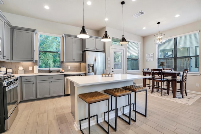 kitchen with gray cabinets, a kitchen island, hanging light fixtures, and appliances with stainless steel finishes