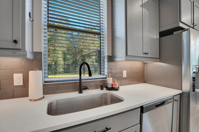 kitchen featuring decorative backsplash, stainless steel appliances, gray cabinets, and sink