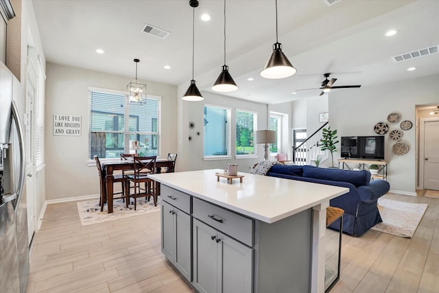 kitchen with a center island, ceiling fan with notable chandelier, stainless steel fridge, gray cabinets, and decorative light fixtures