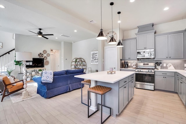 kitchen with ceiling fan, decorative light fixtures, gray cabinets, a kitchen island, and appliances with stainless steel finishes