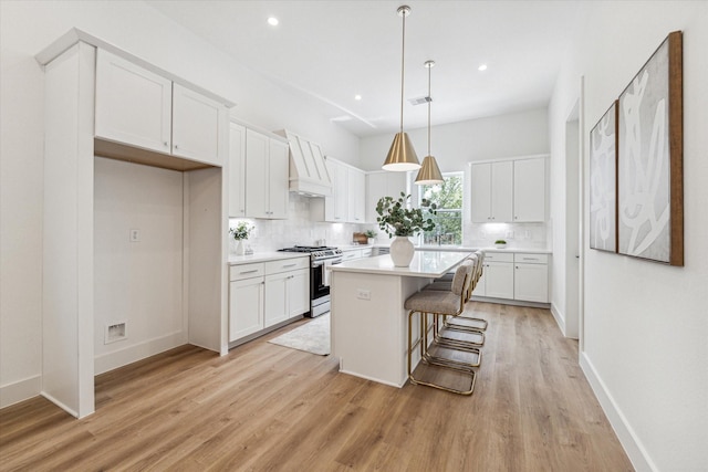 kitchen featuring stainless steel gas range oven, hanging light fixtures, a kitchen island, a kitchen bar, and white cabinetry