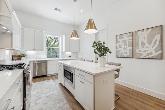 kitchen featuring tasteful backsplash, stainless steel appliances, a kitchen island, pendant lighting, and white cabinetry