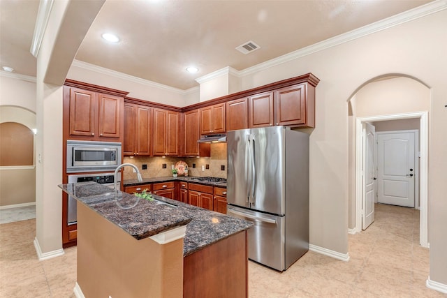 kitchen with sink, dark stone countertops, tasteful backsplash, a kitchen island with sink, and appliances with stainless steel finishes