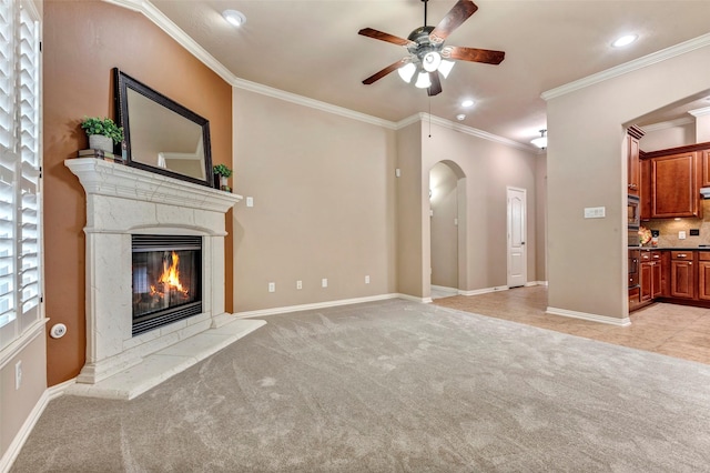 unfurnished living room with ornamental molding, a premium fireplace, ceiling fan, and light carpet