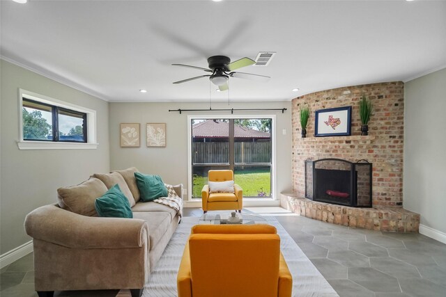 tiled living room featuring plenty of natural light, ceiling fan, crown molding, and a brick fireplace