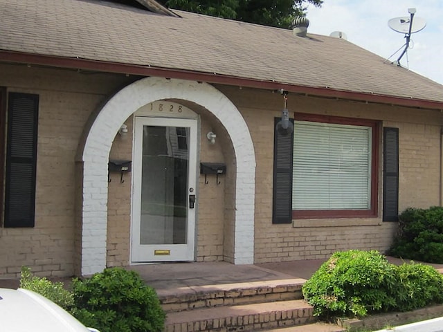 property entrance with brick siding and a shingled roof