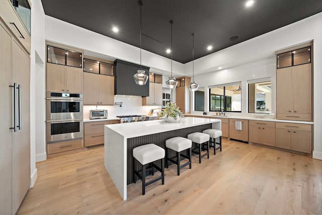 kitchen with a kitchen breakfast bar, hanging light fixtures, light wood-type flooring, appliances with stainless steel finishes, and a large island