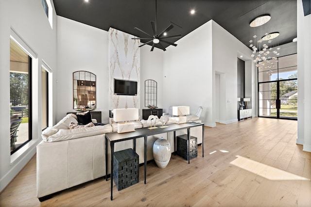 living room featuring light hardwood / wood-style flooring, ceiling fan with notable chandelier, and a high ceiling