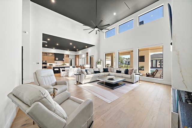 living room with ceiling fan, light wood-type flooring, and a towering ceiling