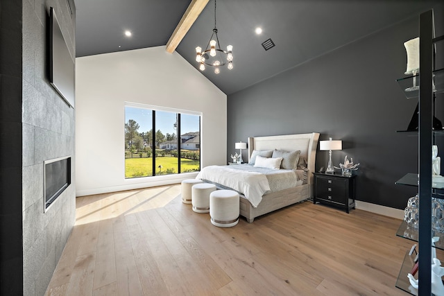 bedroom with a tile fireplace, a chandelier, beamed ceiling, and light hardwood / wood-style floors