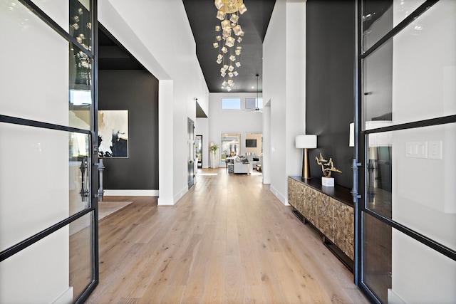 foyer with an inviting chandelier, light wood-type flooring, a towering ceiling, and french doors