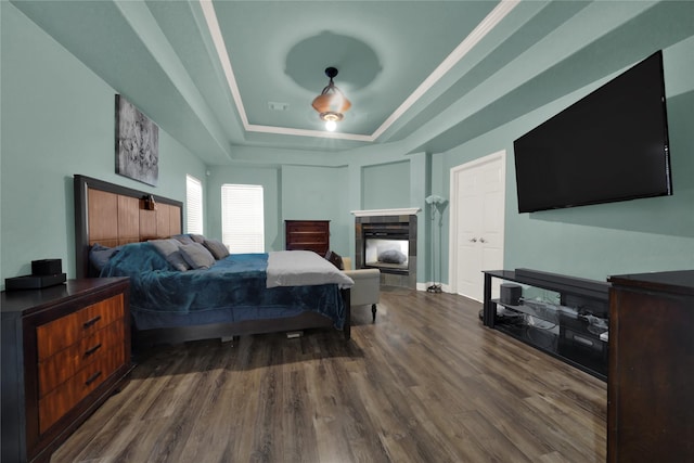 bedroom featuring a fireplace, dark wood-type flooring, and a tray ceiling