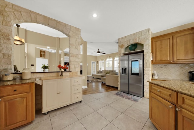 kitchen with stainless steel refrigerator with ice dispenser, backsplash, light stone counters, ceiling fan, and light tile patterned floors