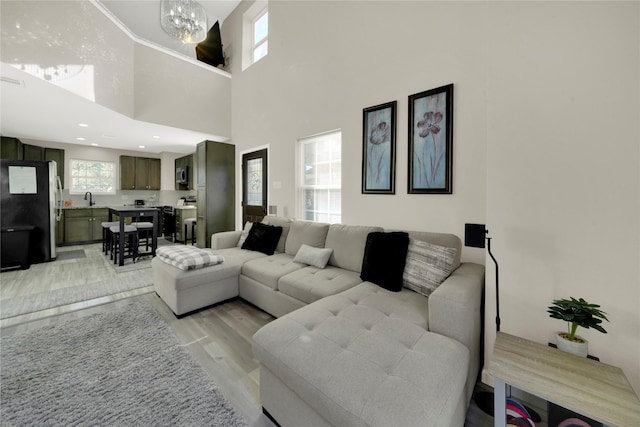 living room featuring sink, a towering ceiling, light hardwood / wood-style floors, and a notable chandelier