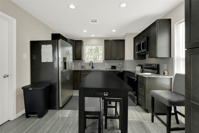 kitchen with sink, light hardwood / wood-style flooring, light stone countertops, dark brown cabinets, and stainless steel appliances