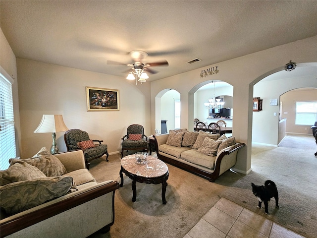 living room featuring light tile patterned floors, ceiling fan with notable chandelier, and a textured ceiling