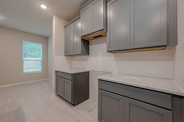 kitchen featuring backsplash, light hardwood / wood-style flooring, light stone counters, and gray cabinetry