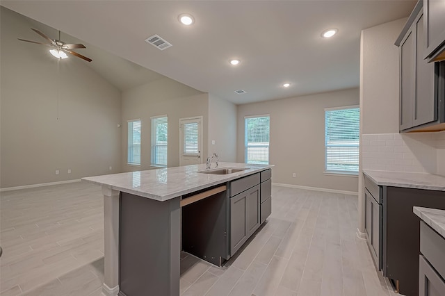 kitchen with gray cabinetry, decorative backsplash, sink, and an island with sink