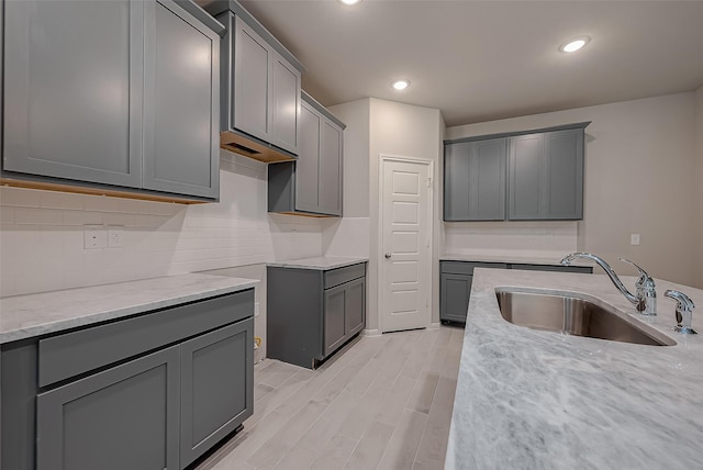 kitchen with light stone countertops, light wood-type flooring, gray cabinets, and sink