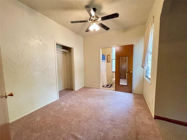 unfurnished bedroom with ceiling fan, a closet, light carpet, and ensuite bath