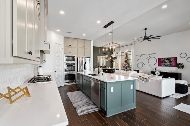 kitchen with appliances with stainless steel finishes, ceiling fan with notable chandelier, sink, pendant lighting, and an island with sink