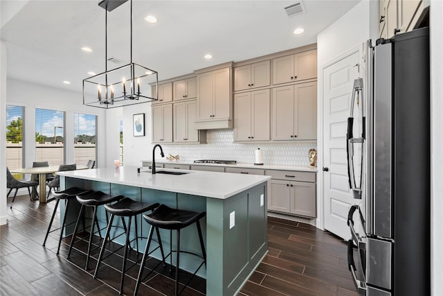 kitchen with a breakfast bar, stainless steel appliances, a kitchen island with sink, sink, and decorative light fixtures