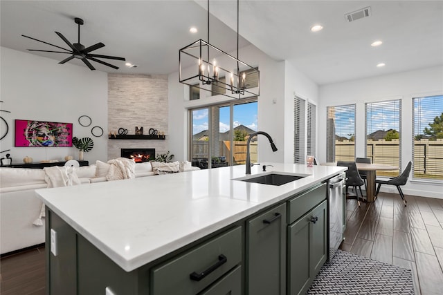 kitchen featuring ceiling fan with notable chandelier, a large fireplace, sink, hanging light fixtures, and an island with sink